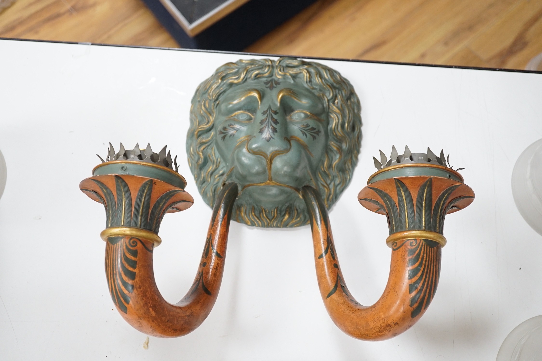 A pair of carved and decoratively painted twin-branch lion mask wall lights with tall glass shades, wall lights 38cms high, shades 32cms high